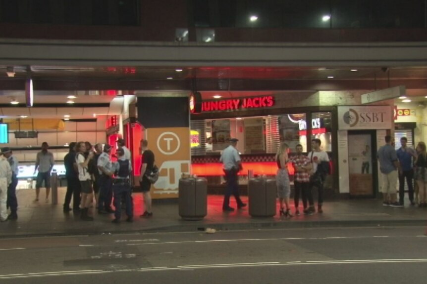 A view from across the road of police talking to witnesses outside Hungry Jack's.