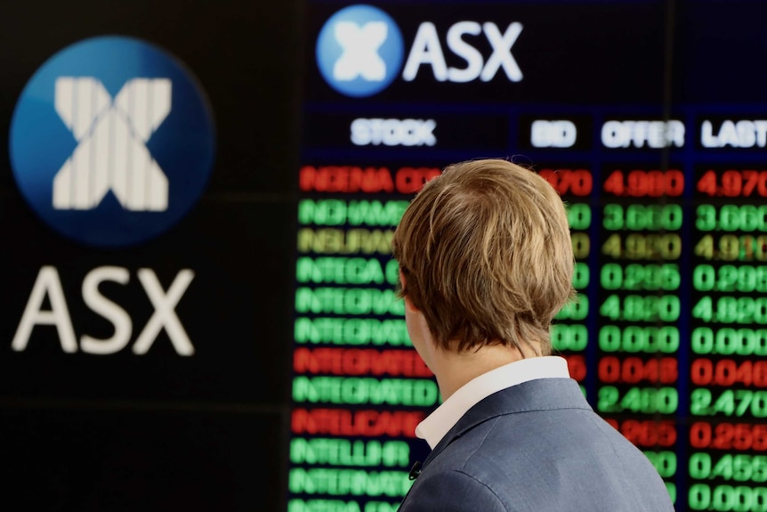 A man in a suit, seen from behind, looks at the ASX share price boards.
