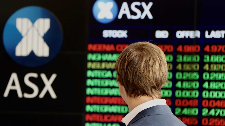 A man, seen from behind, looks at the ASX share price boards.