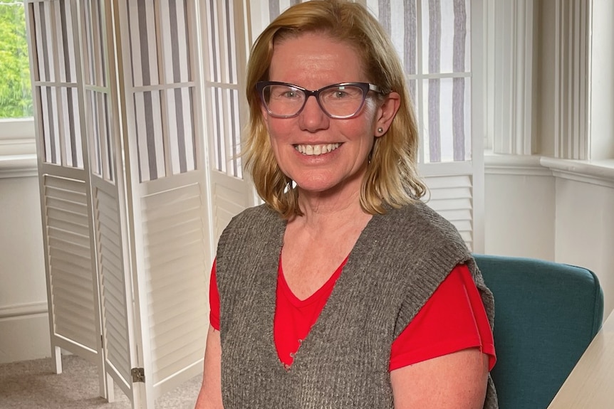 A woman with blonde hair and glasses smiles at the camera