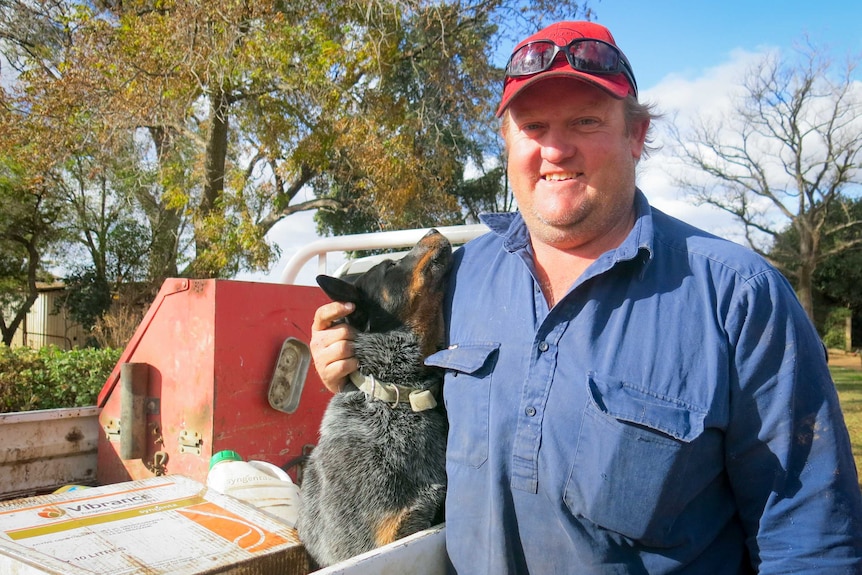 A man scratches his dog's neck standing next to his ute