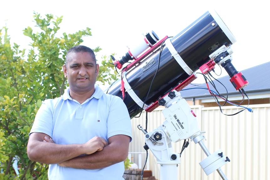 a man in a white polo standing next to a telescope