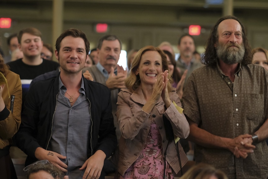 Rows of people stand smiling and clapping in an auditorium