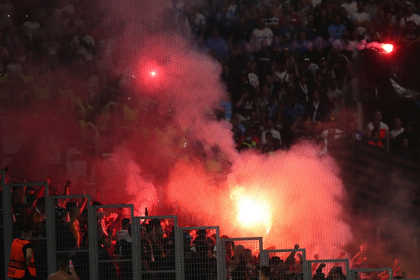 A red flare can be seen with supporters gesturing under the smoke