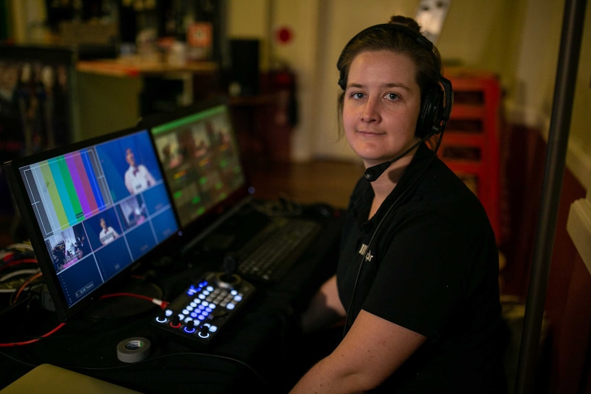 A woman sitting at two monitors with a head set on
