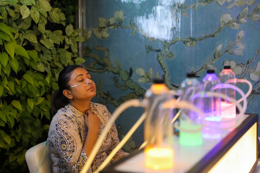 Une femme assise avec des tubes dans le nez, respirant de l'oxygène à partir de petites bouteilles colorées dans un bar à oxygène. 