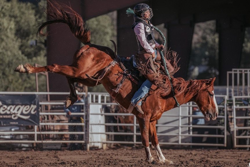 A woman in safety gear rides a bucking bronco.