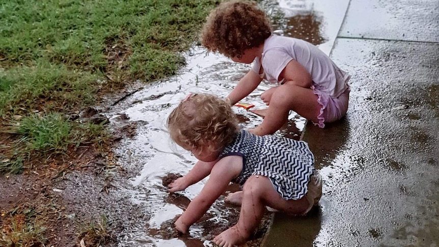 Two girls play in puddles.