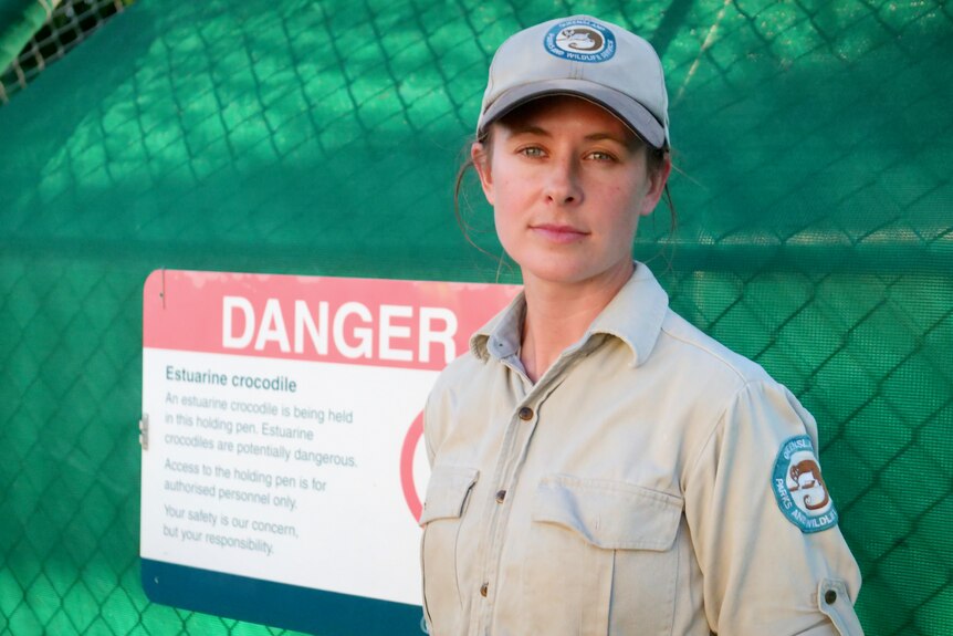 A woman in Queensland Parks and Wildlife Service uniform stands next to a danger sign