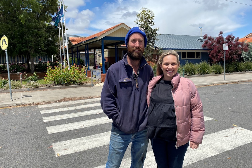 A smiling man and woman, warmly dressed, standing in front of a community building.