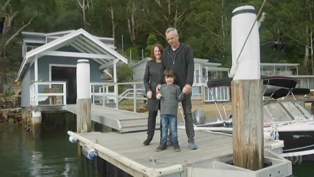 Man, woman and young boy stand on pier in front of small house on river
