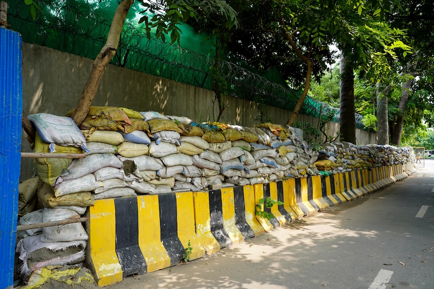 A row of yellow and black bollards line the road, with sandbags stacked up on top leaning against a cement wall
