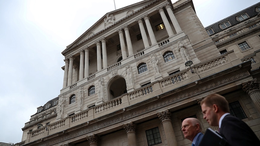Two men wearing suits walk past the Bank of England in London.
