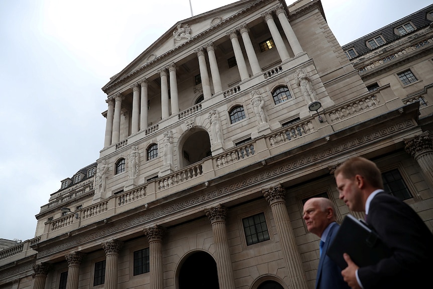 Two men wearing suits walk past the Bank of England in London.