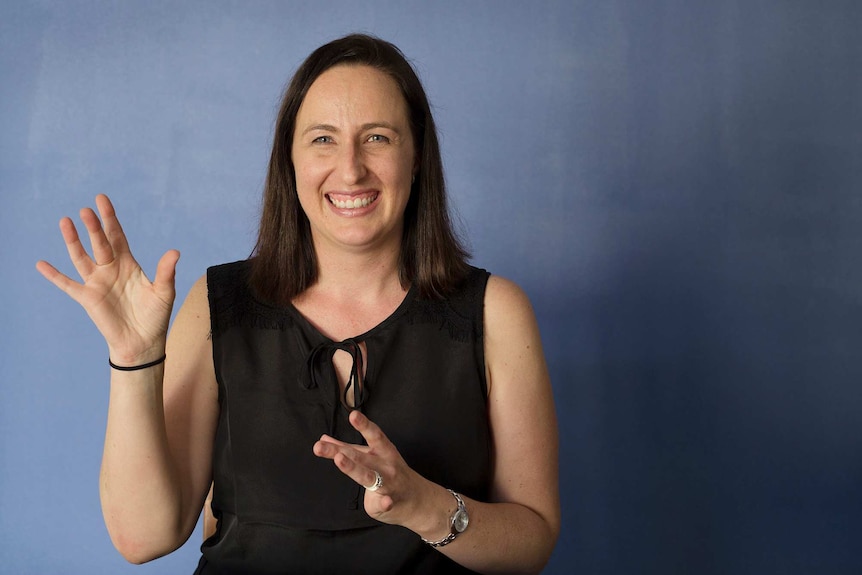 Auslan interpreter Rebecca O'Brien looking into the camera making the sign with her hands for Auslan.