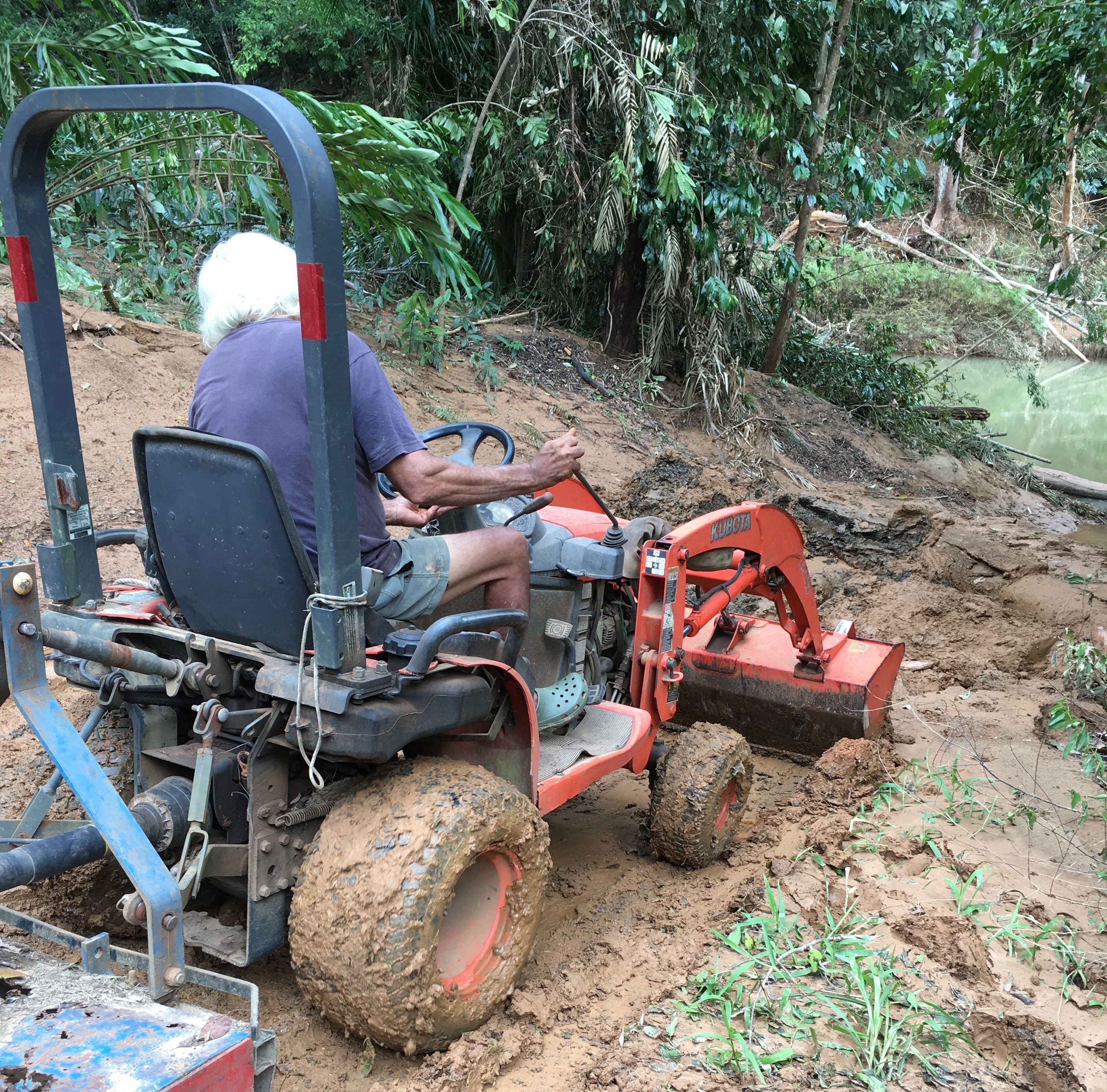A man on a tractor clearing mud and debris on a road