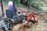 A man on a tractor clearing mud and debris on a road.