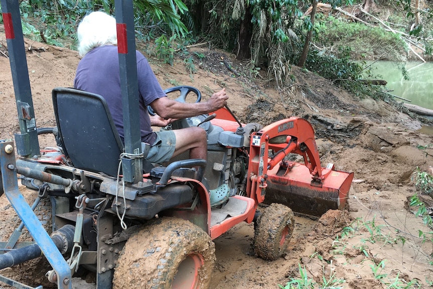 A man on a tractor clearing mud and debris on a road.
