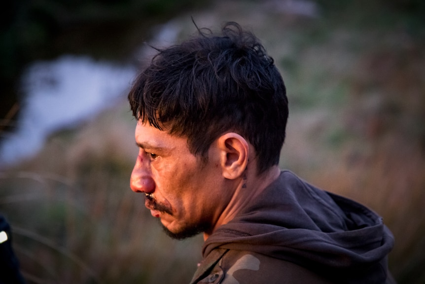 A Samoan man in his 40s with a scar on the bridge of his nose looks to his left, with a troubled expression