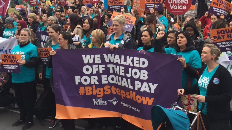 Hundreds of childcare workers rally on the steps of the state library, holding protest signs.