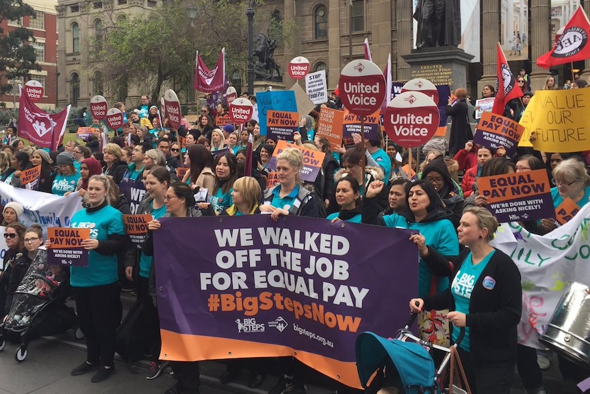 Hundreds of childcare workers rally on the steps of the state library, holding protest signs.