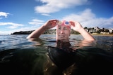 A woman puts on swimming googles while floating in a bay