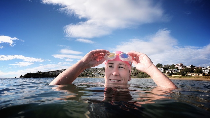 A woman puts on swimming googles while floating in a bay