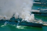 Firefighting boats spray a US Navy ship which has smoke billowing from it.