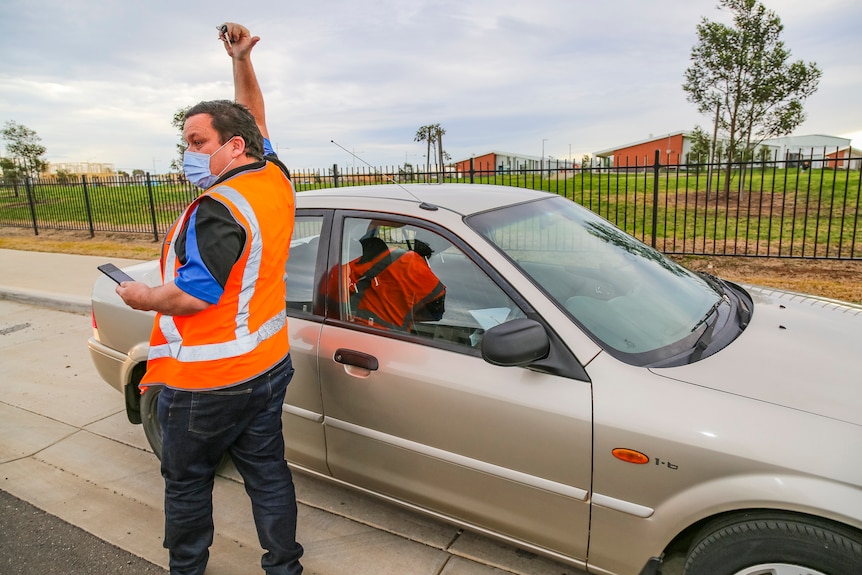 A man in a bright orange high-vis vest signals thumbs up to someone who can't be seen.