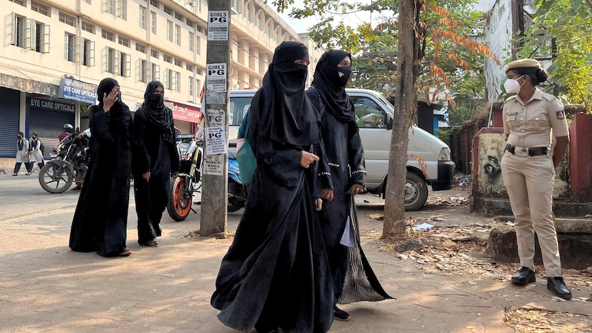 A police officer watches as four Muslim women in black including hijabs arrive at an Indian school