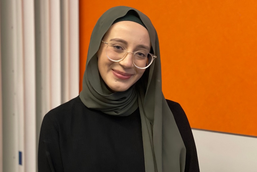 A young woman in a headscarf looks at the camera smiling. 