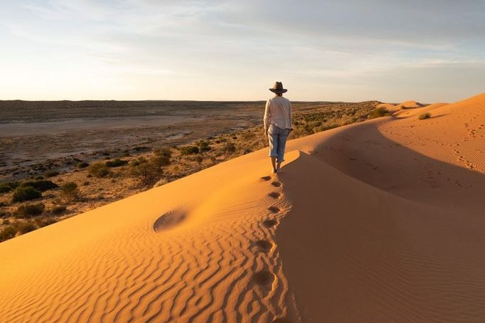 A person walks along a big red sand dune at sunset in outback Queensland.