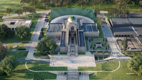 An aerial image of the war memorial with an extension on the back. It sits below a tree-filled mountain