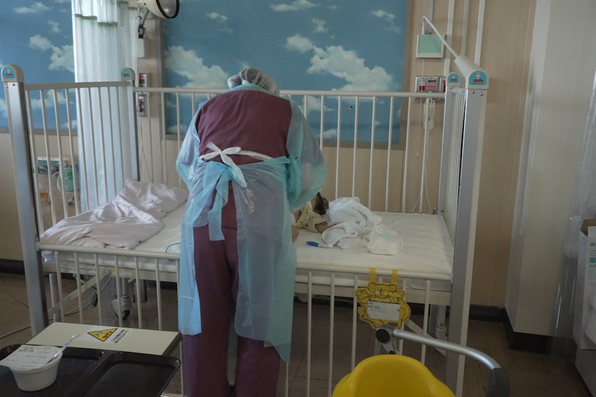 A nurse bending over a cot in hospital changing a baby's nappy 
