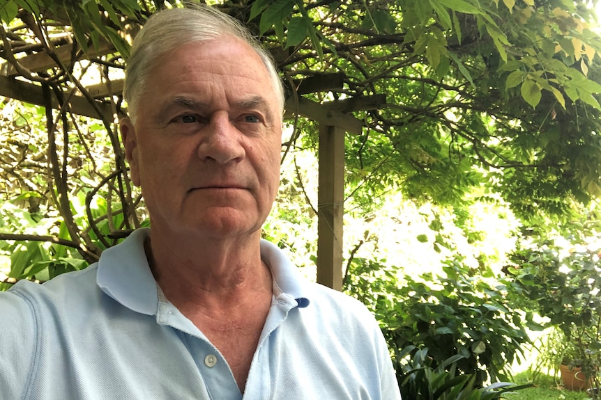 A retired man takes a selfie in front of greenery