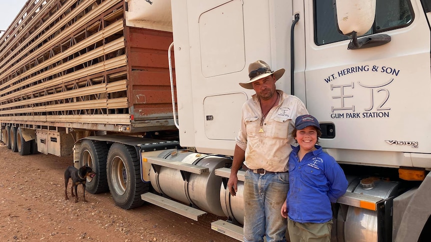 A famer and his son stand in front of a large livestock truck.