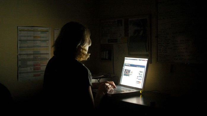 Woman sitting in front of a laptop computer in the dark.
