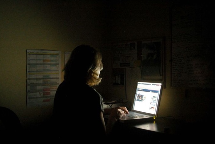 A woman works at her laptop computer late into the night.