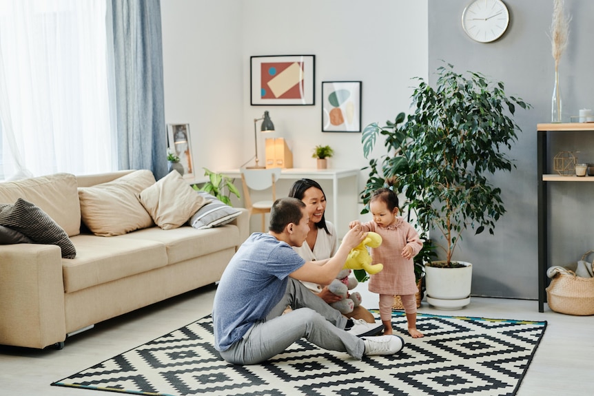 A man and woman sit on a rug playing with a toddler. 