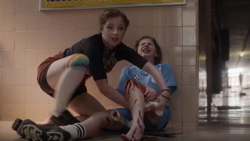 A girl ties a tourniquet around a student's bleeding leg in a scene from a PSA about school shootings.