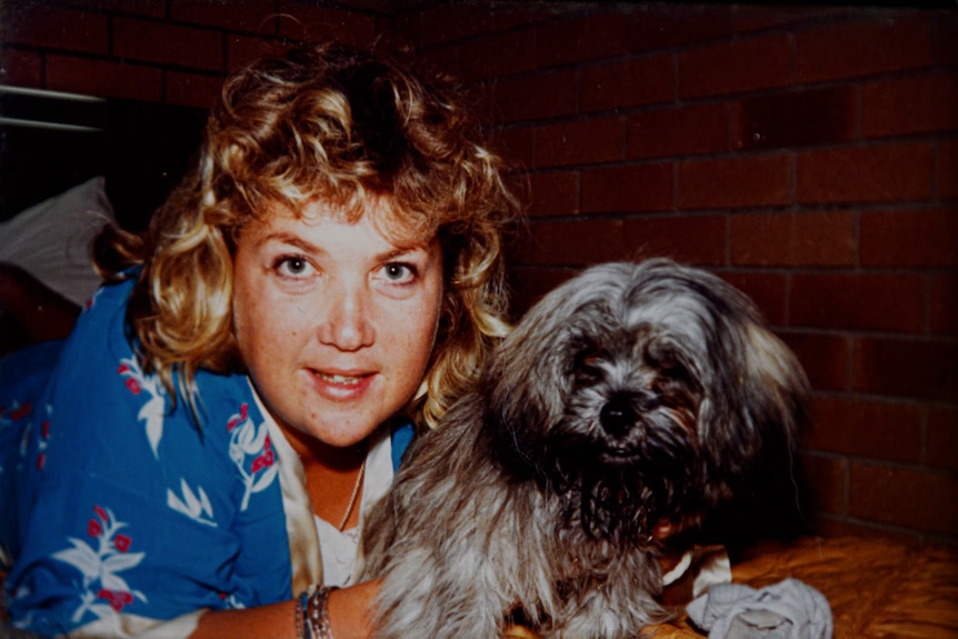An old photo of a woman with curly hair, posing with a small grey dog.