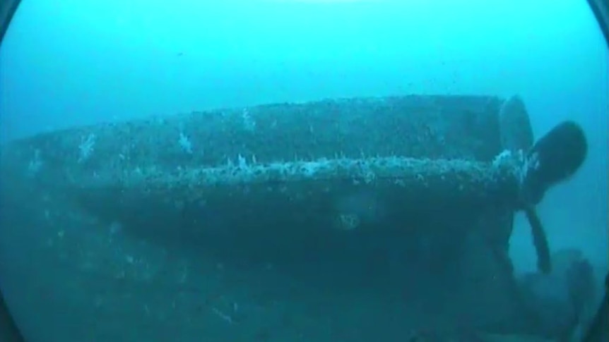 An underwater camera films a sunken shipwreck, with a propeller showing in the shot.
