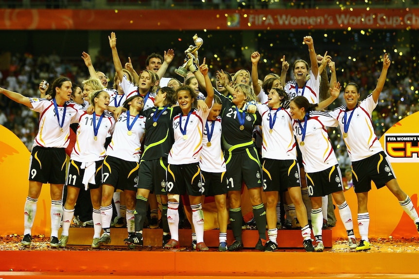 A group of German women footballers dance on a stage while holding a trophy as confetti flies in the air.