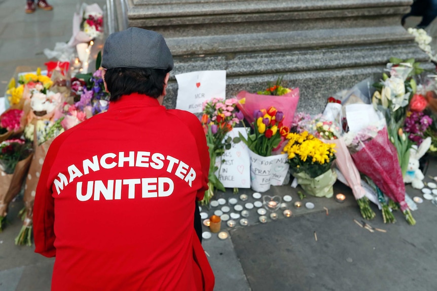 A man in a Manchester United jacket lays flowers at the vigil in Albert Square.