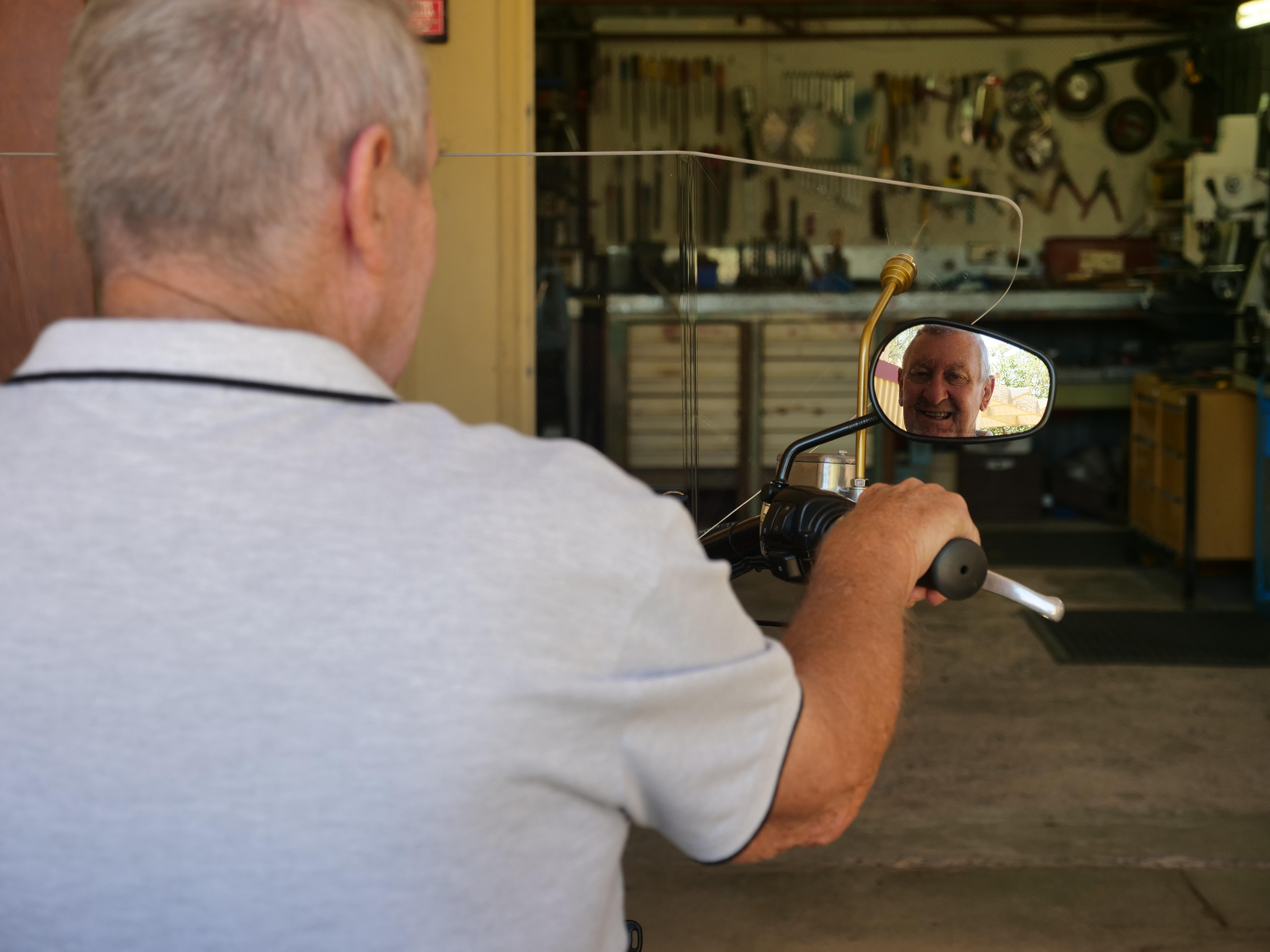 Un hombre con una polo gris mira por el espejo retrovisor. 
