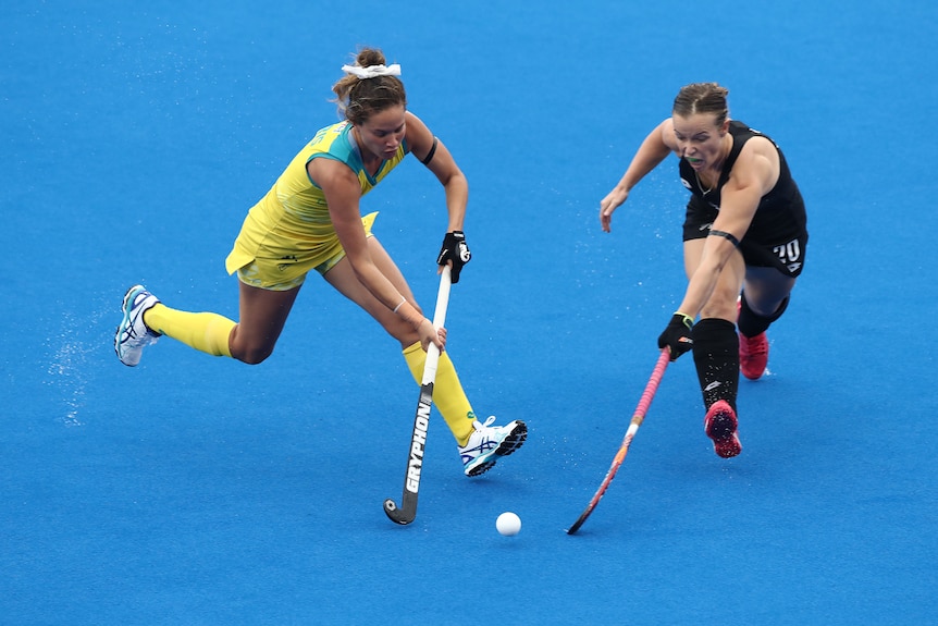 Two female hockey players battle for the ball during a match on blue surface