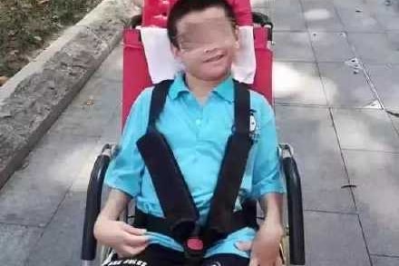 A boy in yellow shirt pushes a wheelchair of another boy in blue shirt sitting in.