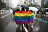 Three people walking holding a rainbow flag behind them