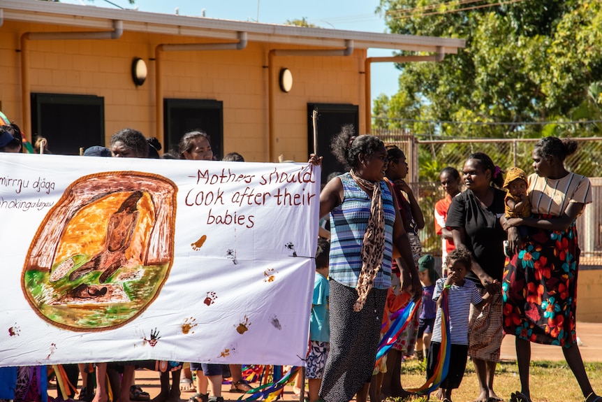 Women hold a banner saying "mothers should look after their babies".