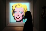 the silhouette of a woman looking at the print hanging on a wall. The print is of Marilyn Monroe's face, highlighted in blue